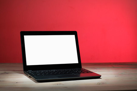 laptop with a clean white screen on the table and a red backgroundの写真素材
