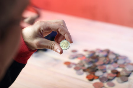 coin two euros in the fingers against the background of a table with coinsの写真素材