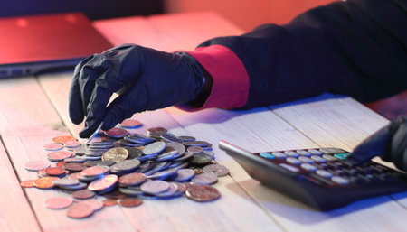 counting old coins by a person in black gloves on a table next to a laptopの写真素材