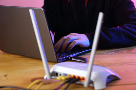 a person typing on a laptop with a modem connected and a blurred router in the foreground