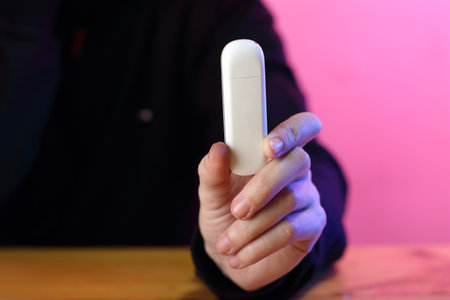 white gsm modem in the fingers of the left hand and against the background of a person in a black sweatshirtの写真素材