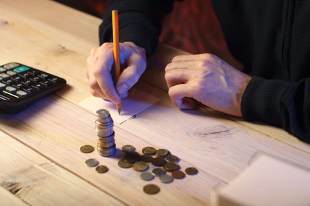 writing down the accrued coins on a piece of paper with a pen by a person on a colored backgroundの写真素材