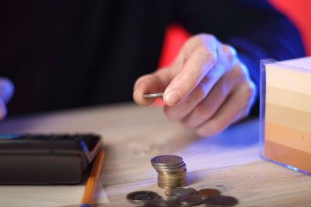 counting coins by a person on a table next to a calculator and a piece of paper with a pen