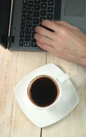 a cup of coffee on the table with a laptop and a hand from aboveの写真素材