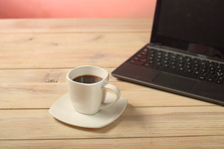 white cup with coffee on the table next to the laptopの写真素材