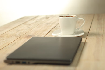 a cup with coffee behind a laptop on a plank table