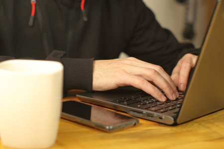a person typing on a laptop next to a smartphone and a cup of coffee