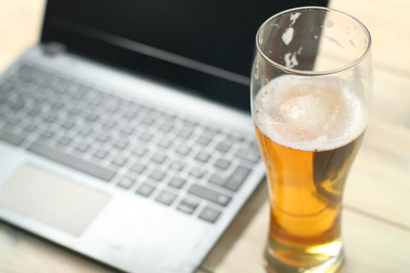 a full mug of beer on the background of a laptop and a wooden table