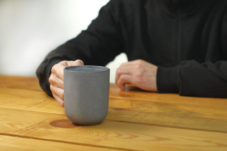 person holding a mug with coffee on a plank tableの写真素材