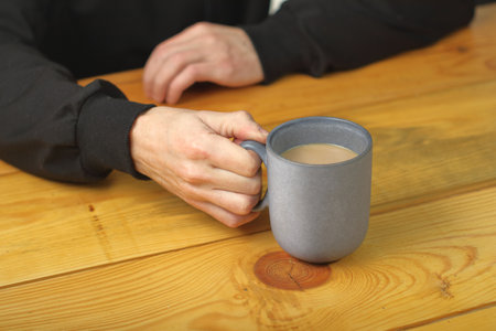 person holding a mug with coffee on a plank tableの写真素材
