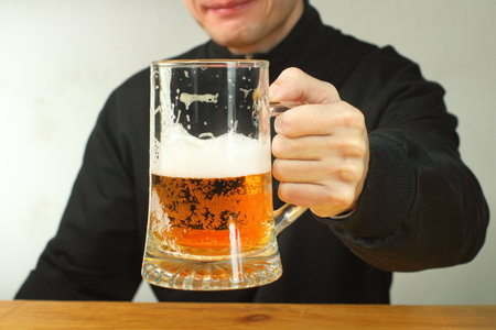 person holding a mug of beer over the tableの写真素材
