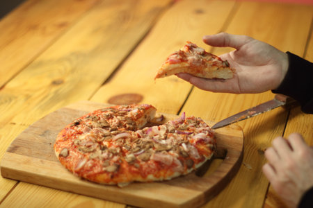 piece of pizza in the hands of a person over the tableの写真素材