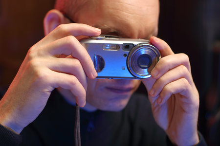 a person holds an old compact camera near the eyes in his hands