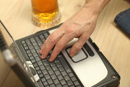 person typing on the keyboard of an old laptop next to a beer mugの写真素材