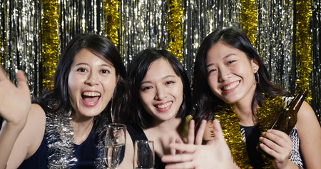 young asian girl teenagers trying alcohols at nightclub in their 20s. ladies in sexy party dresses waving hands to camera enjoying music at club. beautiful women in having fun talking on video chatの写真素材