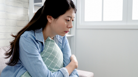 asian woman at home looking sad unhappy and thoughful. Pretty girl sitting on couch in apartment doing nothing feeling depressed. young housewife in a bad mood.の写真素材