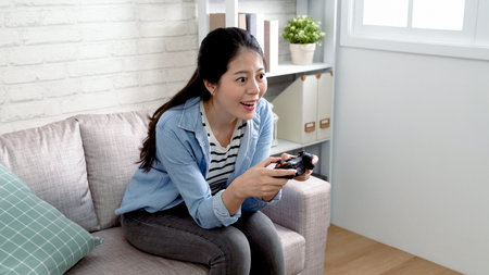 Beautiful asian female playing video games on console having fun. cozy place with comfortable couch...