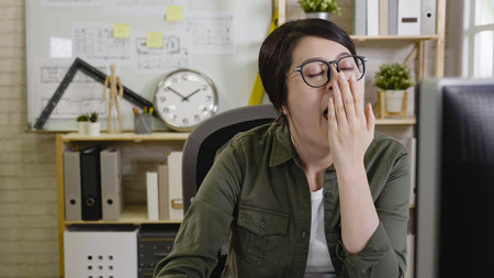 Tired overworked woman architect yawning working on computer .