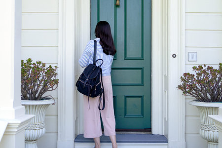 back view of girl college student carrying backpack back to home using key opening door.