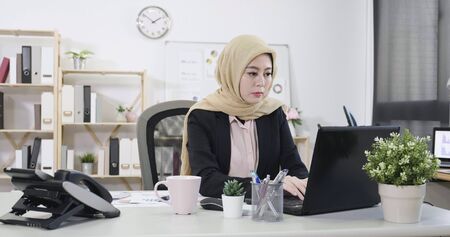 muslim businesswoman sitting in workplace in modern cozy office typing  at notebook pc screen.の写真素材