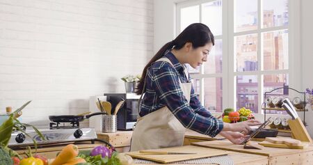Young elegant asian woman in modern kitchen having many green vegetables on island table.の写真素材