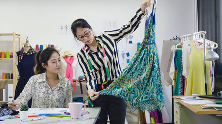 Beautiful fashion designers women colleagues talking and smiling while working in modern cozy...