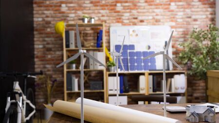 Construction office engineer empty working table. modern eco friendly workplace in architect company indoors with red brick wall. windmill and 3D house miniature on desk for green energy building.の写真素材