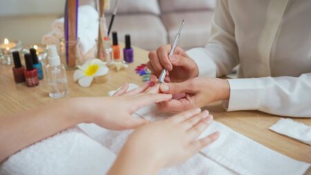 Woman manicurist use nail file drill to cut and fix nail shape of customer in home service beauty treatment. Perfect nails manicure process operation in close up with burst flying debris indoors.の写真素材