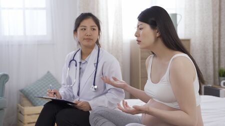 japanese lady having antenatal depression is complaining to psychiatrist during home visit. female consultant listening attentively to her case. pregnancy and mental healthの写真素材