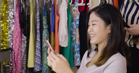 hairdresser work on backstage using curling wand on female model hair. cheerful lady performer laughing and chatting on smart phone in dressing room before show. happy girl enjoy hairstyle processの写真素材