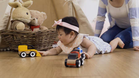 close up adorable baby girl lying on floor is playing with colorful toy cars. cute young kid looking at vehicle models curiously and crawling toward them to touch them.の写真素材