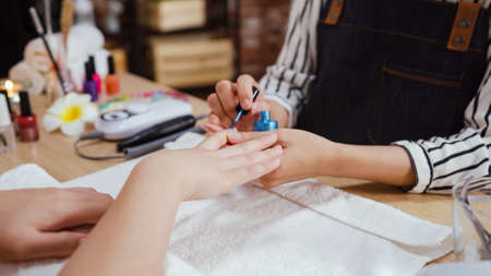 Manicure nail paint blue color in beauty salon. unrecognized manicurist woman in apron sitting at desk and working with customer hands. beautician applying color nail polish to client in studioの写真素材
