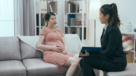 insurance agent in suit visiting pregnant customer at home living room. sales woman explaining...