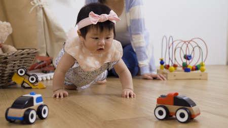 chinese woman playing toys with her daughter in the game room. innocent baby girl attracted by car models pushed out by her mother and crawling forward to catch it.の写真素材