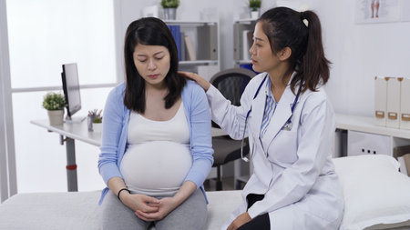 asian pregnant lady crying and complaining to her psychiatrist on clinic couch, covering face with...