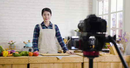 female blogger recording video on live streaming broadcast on social media with professional camera in modern kitchen.の写真素材