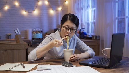 busy asian chinese businesswoman eating unhealthy fast food and looking at document papers while...