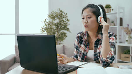 diligent asian japanese girl looking at screen with headphone is self-learning in living room to enhance her english.の写真素材