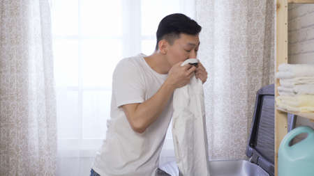 asian chinese guy taking shirt out of machine, smelling collar, amazed at the cleanser works and likes its fragrance in morning at home.の写真素材