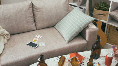 messy living room after a riotous drinking party with empty wine bottles, poker cards and snacks everywhere.の写真素材