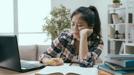 fast forward frowning asian chinese college student feeling studying is tedious and boring during daytime at home.の写真素材
