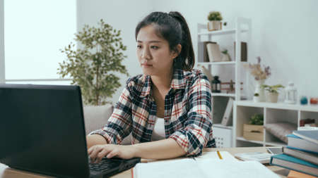 asian japanese millennial woman freelancer writing email to her customer while working on laptop computer with full attention in the morning at homeの写真素材