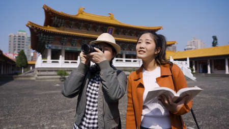 happy female traveler visiting the Confucian temple in Taiwan with her friend is capturing landscape photos in the distance with a digital camera.の写真素材