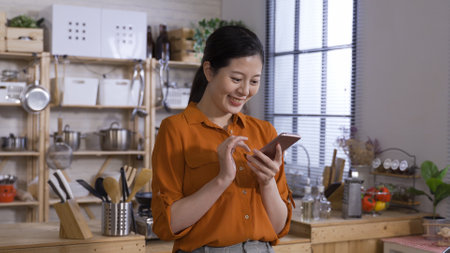 waist up cheerful korean female is having fun while browsing social media feeds on her smartphone in the morning at home.の写真素材