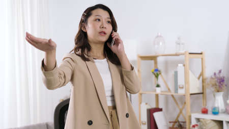 asian businesswoman using hand gestures while explaining something to her customer on mobile phone. authentic lifestyleの写真素材