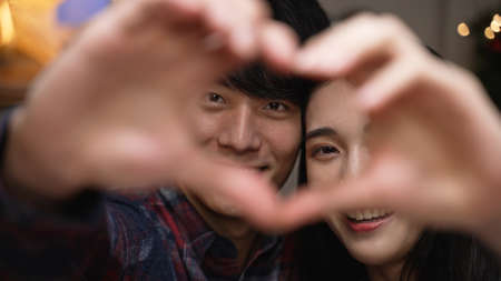 Happy young couple in love showing heart with their fingers and face camera smiling. cheerful girl and boyfriend looking at lens close up view smiling with love gesture on handsの写真素材