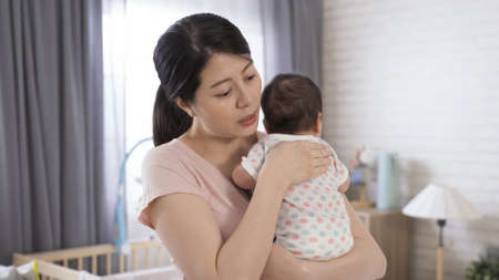 japanese first time mom is adjusting her position to hold properly while burping her baby girl in the nursery room at home.の写真素材