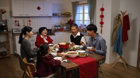 happy asian extended family laughing at the manâs joke while having reunion dinner on chinese new yearâs eve in a cozy festive home interiorの写真素材