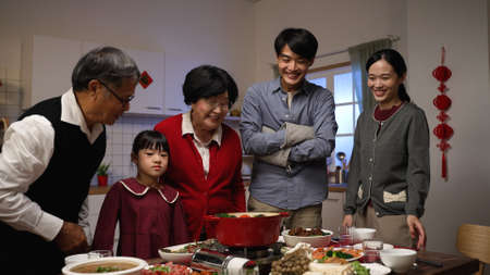 smiling asian father serving hot soup on the dining table and posing with folded arms, feeling proud of his cooking. preparing food for family on lunar new yearâs eveの写真素材