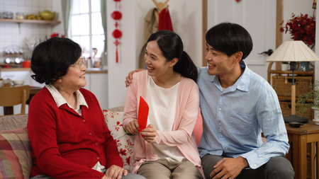 thankful asian young couples giving lunar new year red packet to senior mother during their visit on...